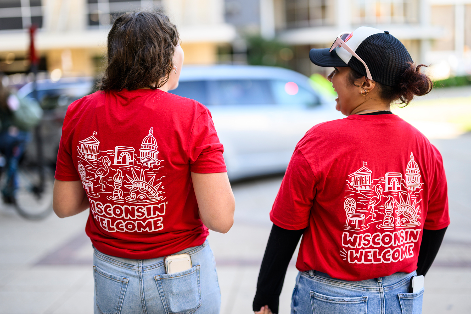 The backs of two people in red "Wisconsin Welcome" t-shirts talking and laughing together.