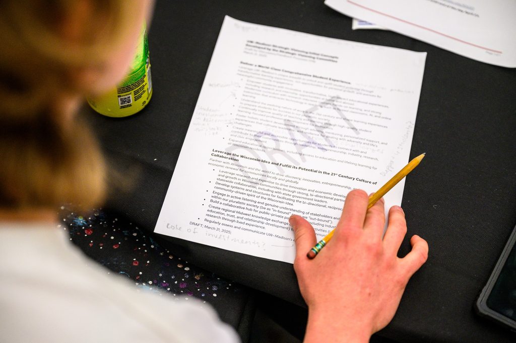 A person reviews a printed draft document at a table while holding a pencil, with handwritten notes in the margins.