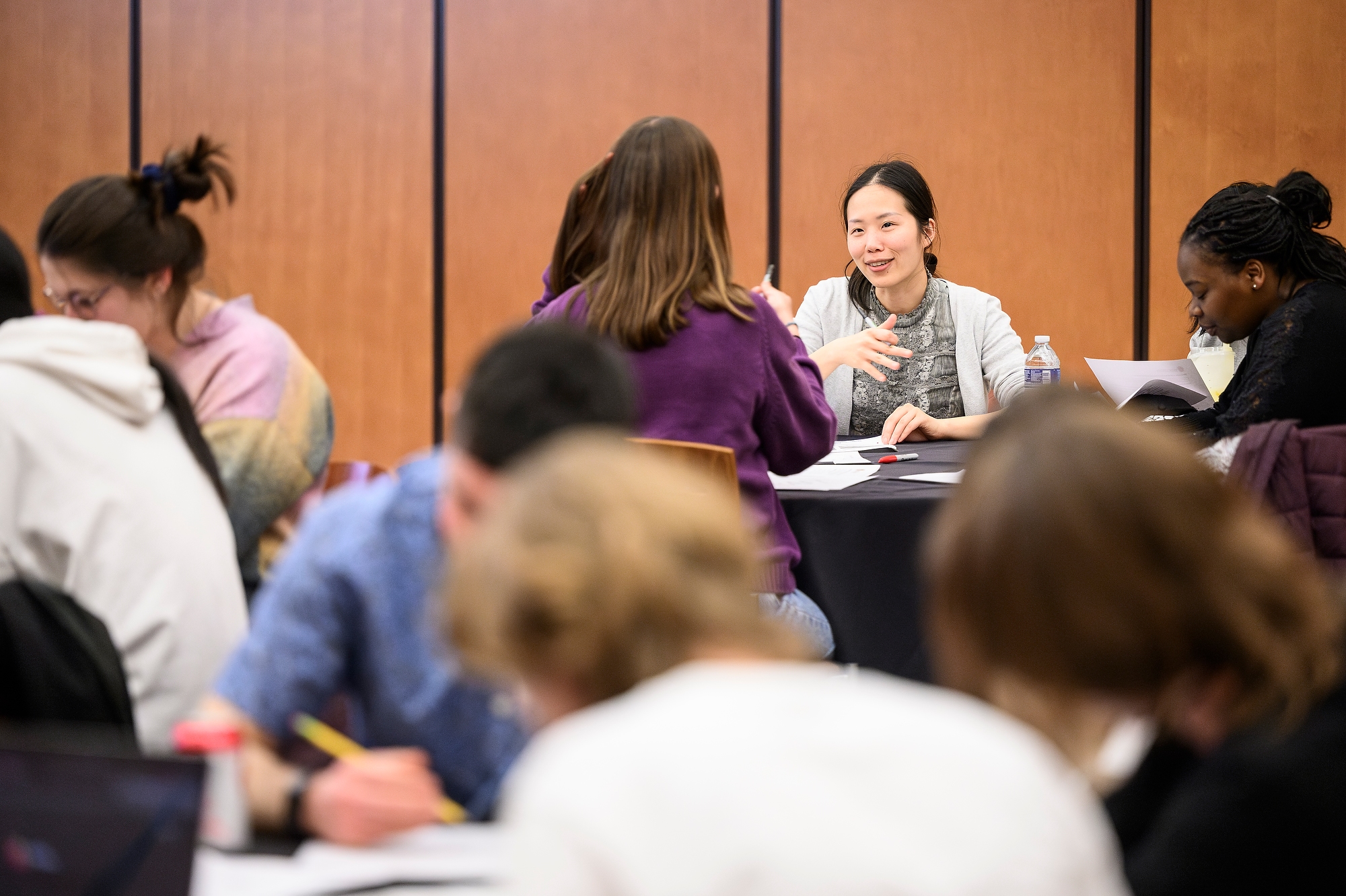 A small group sits around tables in a workshop setting, discussing and giving feedback during a campus event.