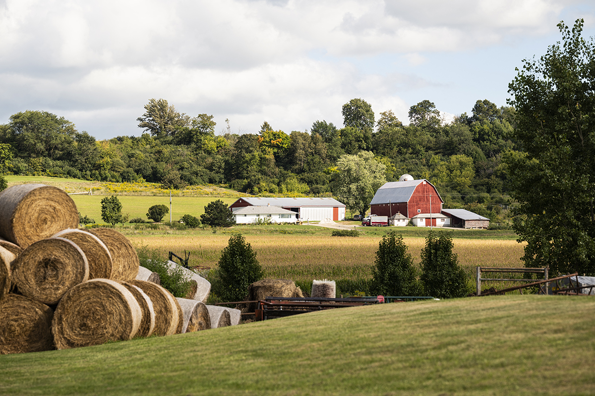 Farm landscape with round bales for hay and a red barn.