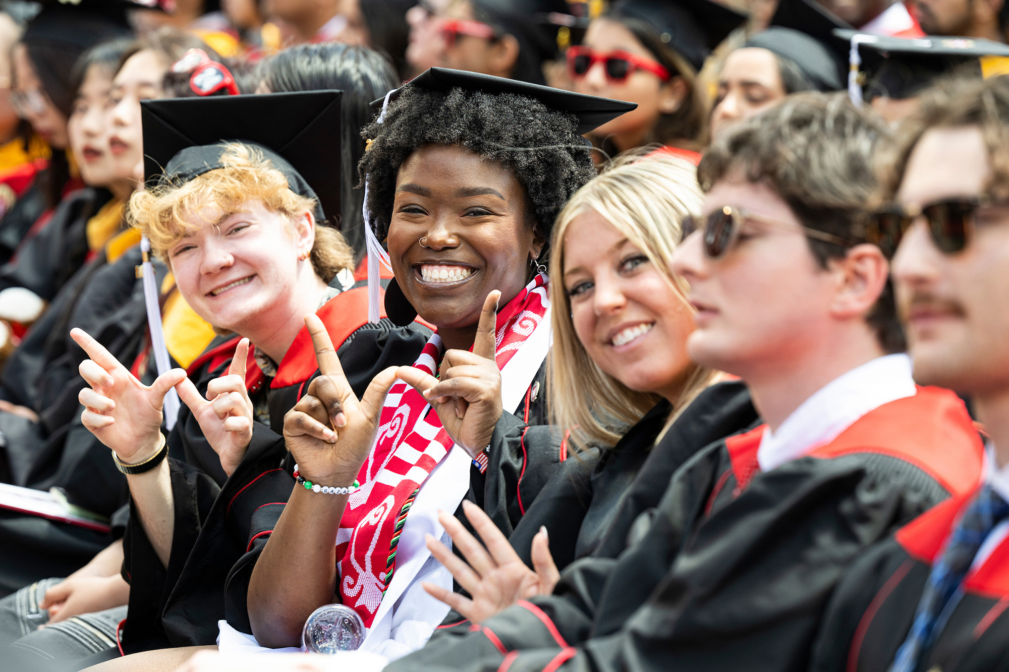 Three graduates with cap and gowns smiling for the camera. Two of them make a "W" with their fingers.