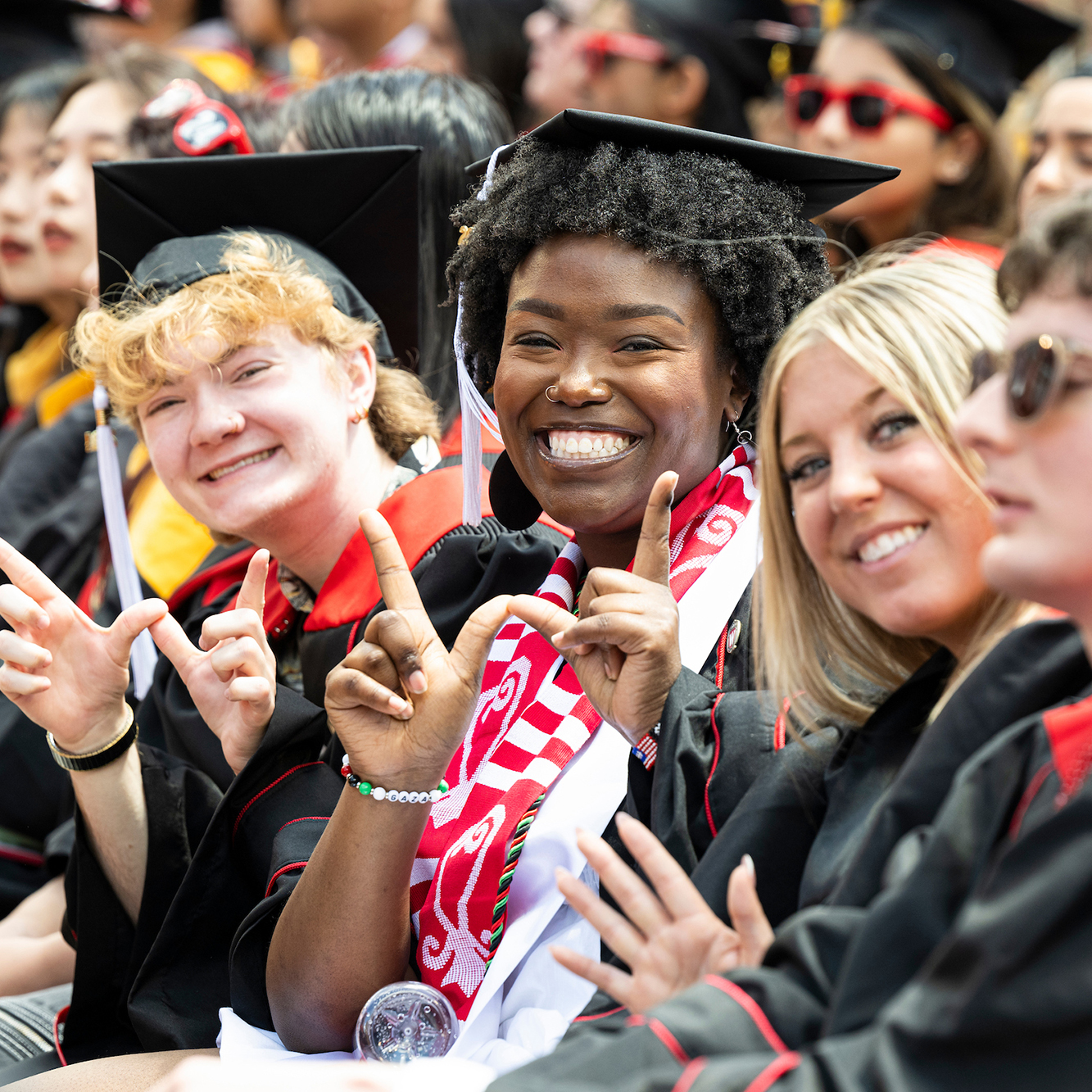 Three graduates with cap and gowns smiling for the camera. Two of them make a "W" with their fingers.